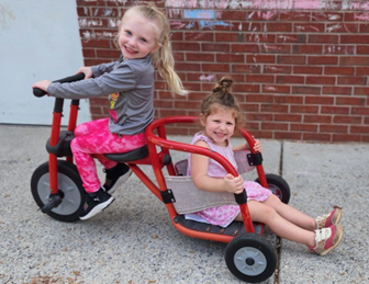 Two girls riding a tricycle

AI-generated content may be incorrect.